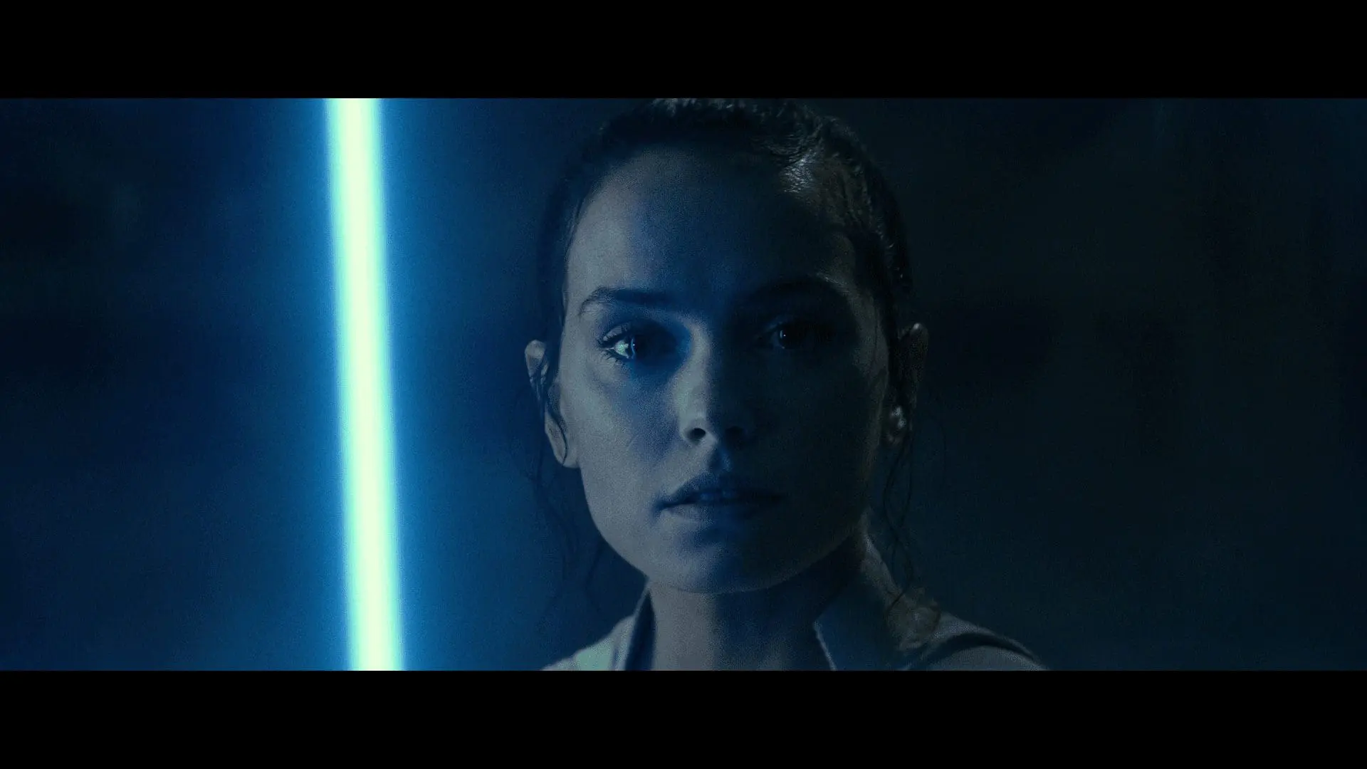 Rey bathed in blue saber light, listening